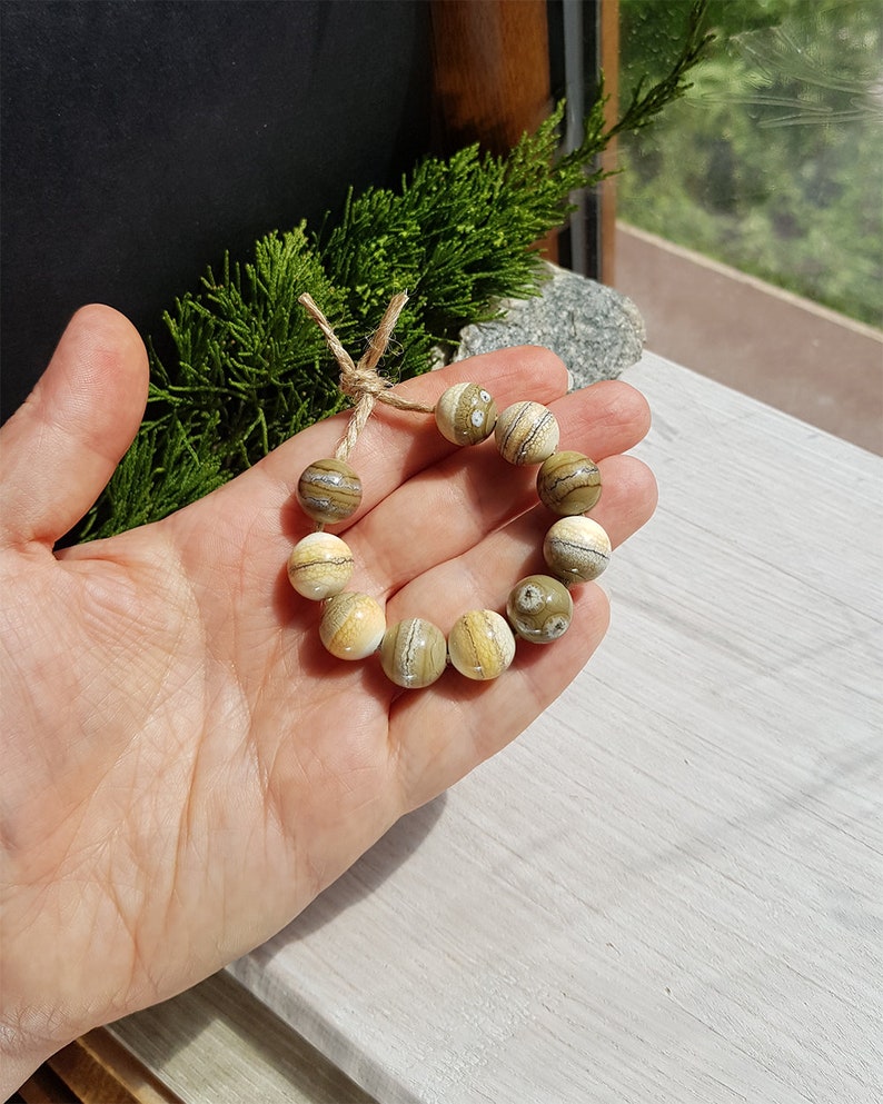 May include: A bracelet made of light brown and cream colored beads with a natural stone pattern. The beads are strung on a twine cord and tied together with a simple knot.