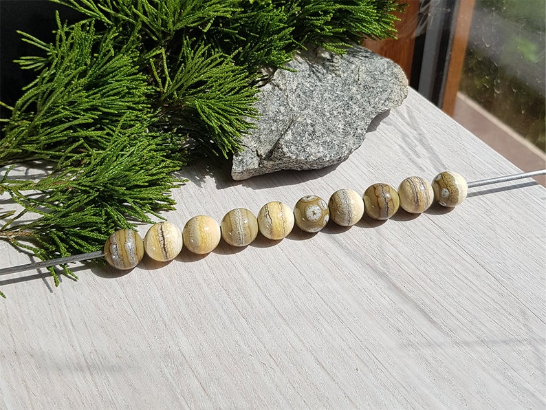 May include: A strand of round, cream-colored beads with brown and white stripes. The beads are strung on a silver wire.
