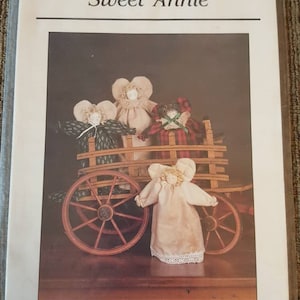 May include: A package featuring a pattern for "Sweet Annie" dolls. The image shows several angel dolls in a wooden wagon. The package is labeled "thimbleberries" with an address.