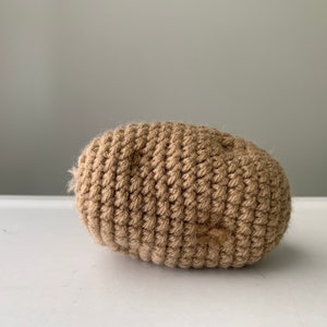 May include: A crocheted brown potato shaped toy. The toy is made of a soft, textured yarn.