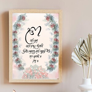 May include: A framed watercolor painting with a floral border and a mandala design. The painting features a quote in Punjabi script: "ਮਤਿ ਨਾਮੁ ਨਿਰਵੇਦ ਅਕਾਲ ਮੂਰਤ ਅਧਾਨੀ ਸੋਨੁੰ ਗੁਰ ਪ੍ਰਸਾਦਿ ॥".