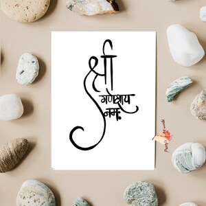 May include: A white card with black calligraphy that reads "Shree Ganeshay Namah". The card is surrounded by small, gray and white stones.