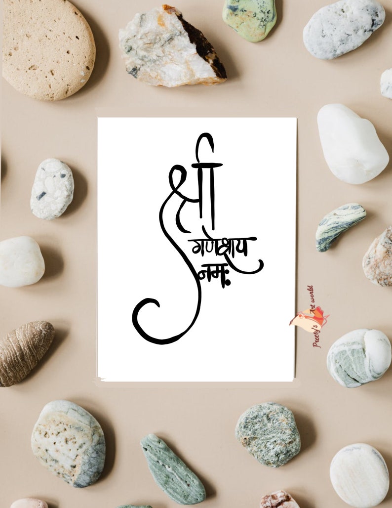 May include: A white card with black calligraphy that reads "Shree Ganeshay Namah". The card is surrounded by small, gray and white stones.