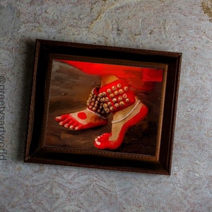 May include: A framed painting of a foot wearing a red anklet with gold bells. The foot is painted in a red color with a white dot on the big toe.