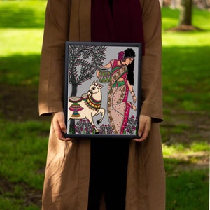 May include: A framed illustration of a woman in a colorful sari carrying a pot, walking with a decorated cow in a green field. The artwork is done in a folk art style with intricate details.