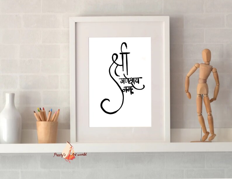 May include: A white framed print with black calligraphy that reads "Shri Ganeshay Namah". The print is displayed on a white shelf with a wooden figurine and a vase.