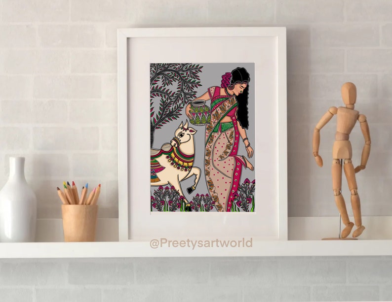May include: A framed illustration of a woman in a colorful sari carrying a pot on her head, walking with a white cow in a field. The background is a gray and green landscape with flowers. The artwork is signed "@Preethysartworld".