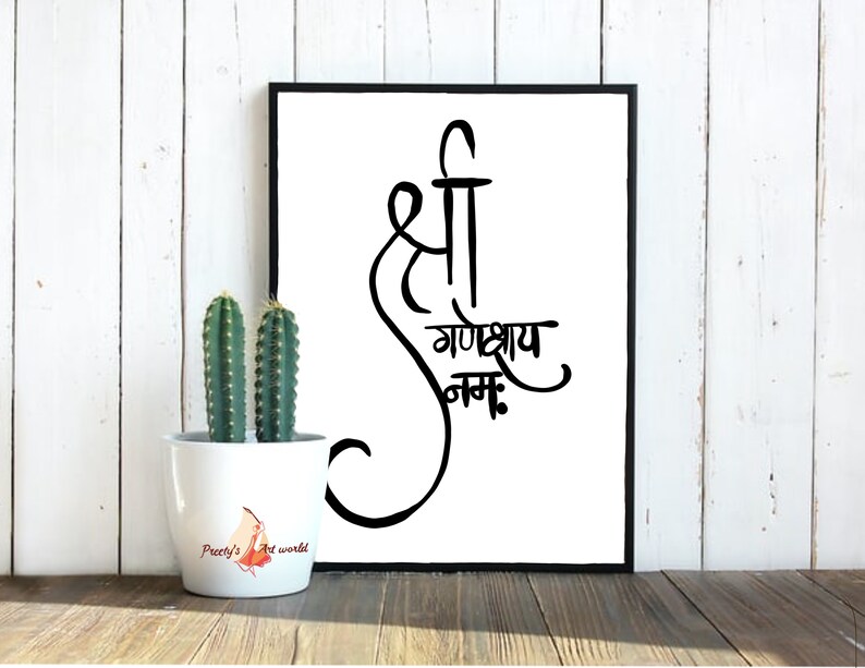 May include: Black and white calligraphy print with the text "Shree Ganeshay Namah" in a decorative font. The print is framed in a black frame and is displayed on a white wooden wall.