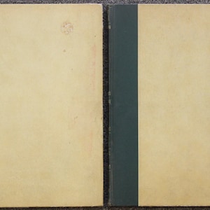 May include: A closed book with a green spine. The book cover is a light beige color.