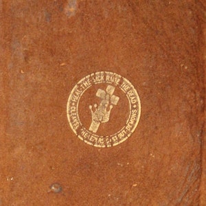 May include: A worn, brown leather-bound book with a gold emblem. The emblem features a cross, crown, and text that reads "Heal the Sick, Raise the Dead, Cleanse Demons, Helpers Cast Out Demons."