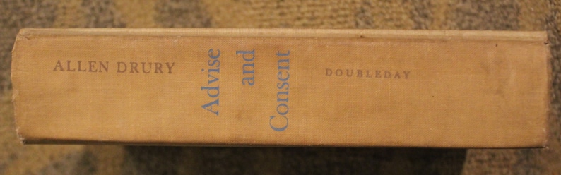 Op de afbeelding: Een bruine boekrug met de titel "Advise and Consent" van Allen Drury en de uitgever Doubleday.