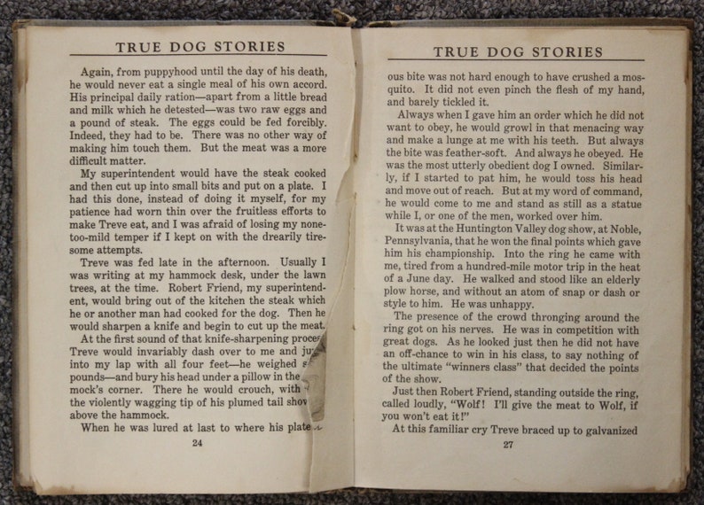 May include: A black and white vintage book with the title "True Dog Stories" printed on the cover. The book is open to pages 24 and 27, showing text about a dog named Treve and his owner's experiences training him.