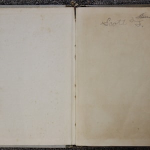 May include: An open book with a blank left page and a handwritten inscription on the right page that reads "Scott J. Flavin".