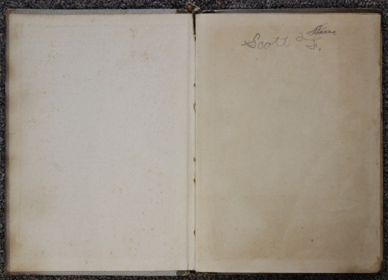 May include: An open book with a blank left page and a handwritten inscription on the right page that reads "Scott J. Flavin".
