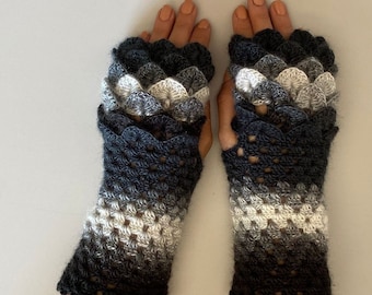 May include: A pair of black, white, and gray fingerless gloves with a crocheted design. The gloves have a scalloped edge and a gradient pattern.