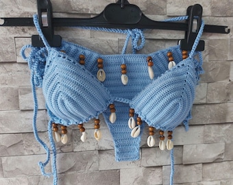 Puede incluir: Un top de bikini de crochet azul claro con cuentas de madera marrón y detalles de conchas blancas.