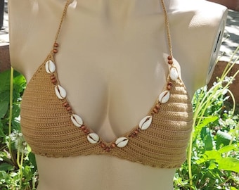 Op de afbeelding: Een bruin gebreid bikini-topje met witte schelpaccenten en bruine kralen. Het topje heeft een driehoekige vorm en verstelbare bandjes.