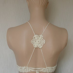 May include: White crochet halter top with a floral design on the back. The top has adjustable straps and ties at the back.