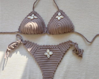 May include: A brown crocheted bikini with white shell embellishments. The top is a triangle style and the bottom is a high-waisted style.