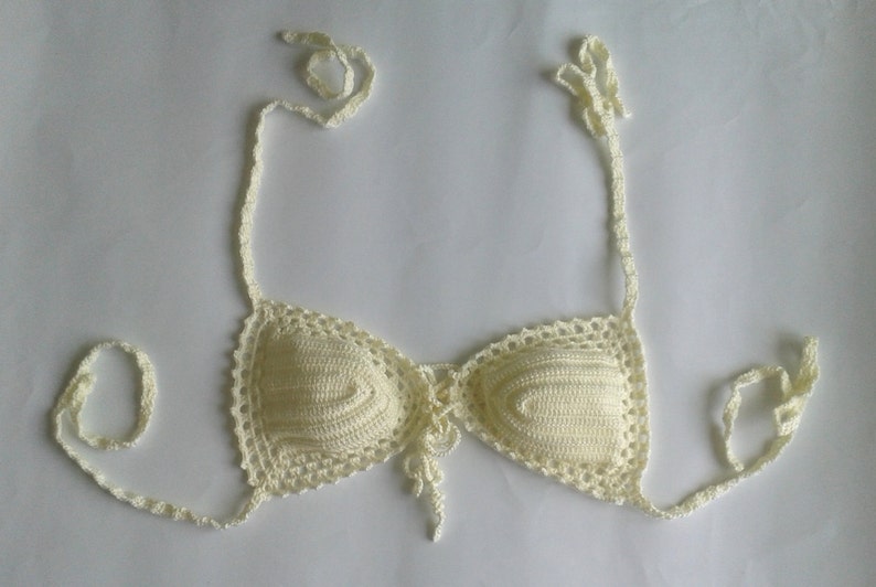 May include: A white crocheted bikini top with adjustable straps. The top has a lace trim and a tie in the front.