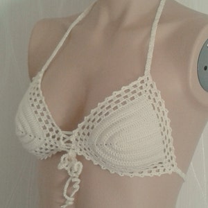 May include: White crocheted bikini top with a halter style strap and a tie at the front.