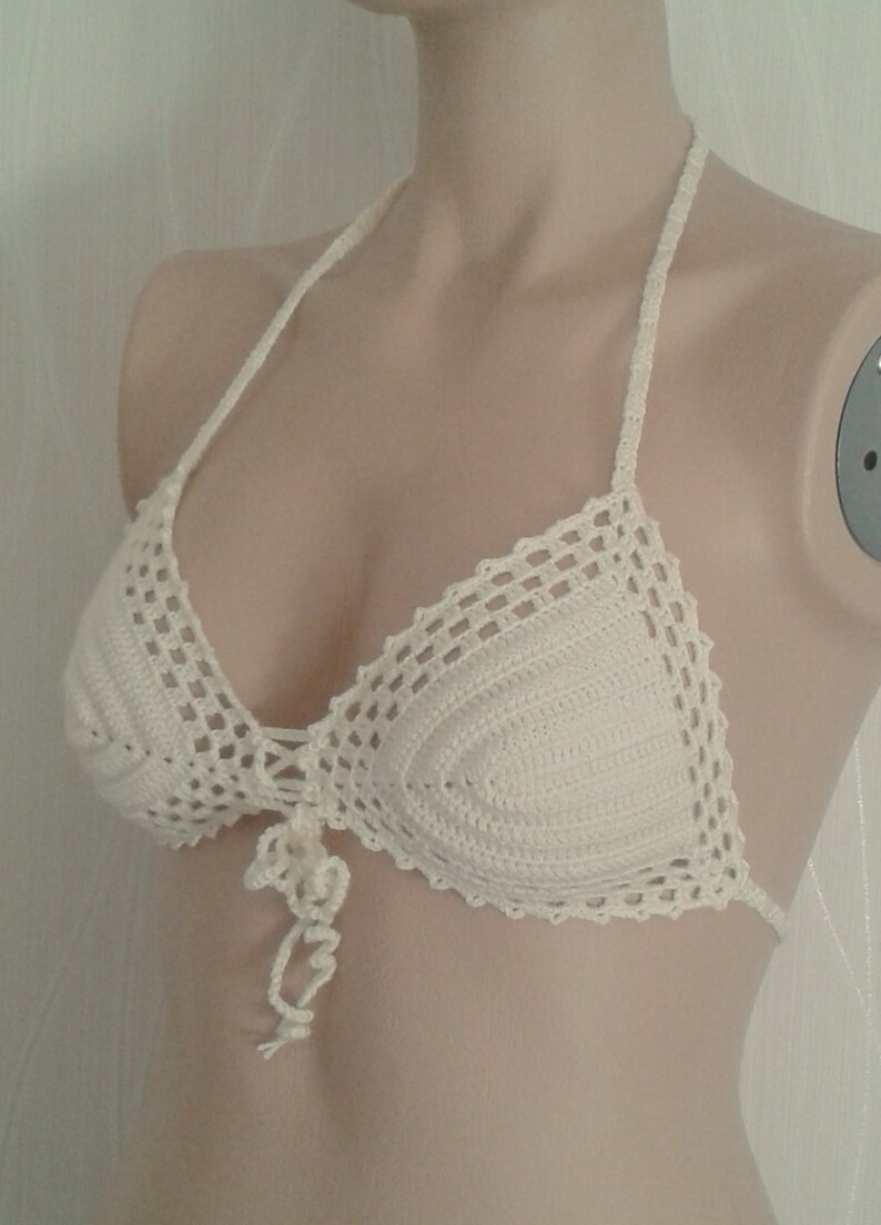 May include: White crocheted bikini top with a halter style strap and a tie at the front.