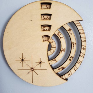 May include: A wooden calendar with a spiral design. The calendar features the months of December, January, February, and the days of the week. The calendar is made of light brown wood and has a starburst design on the bottom.