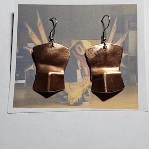 Könnte beinhalten: Ein Paar Ohrringe aus Kupfer mit geometrischer Form. Die Ohrringe haben eine gebürstete Oberfläche und hängen an silbernen Haken.