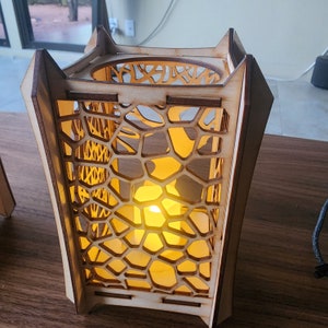 May include: A wooden lantern with a geometric design and a warm light shining through the intricate pattern.