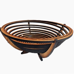 Puede incluir: Un cuenco de madera con un diseño único en capas. El cuenco está hecho de madera natural y tiene una mancha marrón oscura. Es una pieza decorativa que se puede utilizar para servir o como centro de mesa.