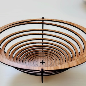 Può includere: Una ciotola di legno con un design a spirale. La ciotola è realizzata con più strati di legno impilati uno sopra l'altro. La ciotola è di colore marrone e ha una finitura in legno naturale.