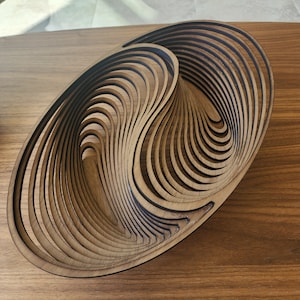 May include: A wooden bowl with a unique, swirling design. The bowl is made of thin, layered pieces of wood that create a three-dimensional effect.