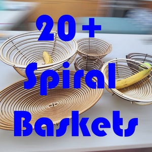 Könnte beinhalten: Eine Sammlung von über 20 spiralförmigen Holzkorben in verschiedenen Größen. Die Körbe bestehen aus dünnen Holzstreifen, die miteinander verwoben sind, um ein Spiralmuster zu erzeugen. Einige der Körbe sind mit Obst gefüllt, wie zum Beispiel Bananen.