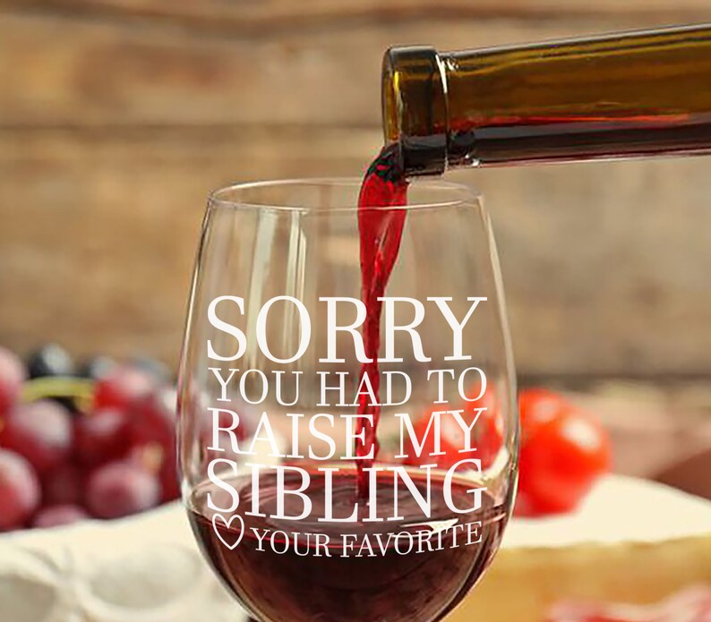 May include: A clear wine glass with the text "Sorry you had to raise my sibling" and a heart with the text "Your Favorite" printed on it. Red wine is being poured into the glass.