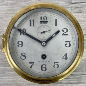 May include: A brass clock with a white face and black hands. The clock has Roman numerals and a small second hand. The clock face also has the text "中华人民共和國" in Chinese.