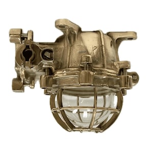May include: Brass industrial style wall light fixture with a clear glass globe and a cage. The light has a mounting bracket and a swiveling arm.