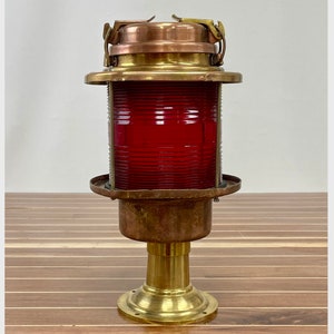 May include: A brass and copper nautical navigation light with a red lens. The light is mounted on a brass base.