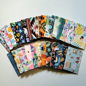 May include: A collection of rectangular fabric card holders arranged in a fan shape. Each holder features a unique pattern, including floral prints, geometric shapes, animal motifs, tropical pineapple designs, and seasonal holiday themes in various colors.