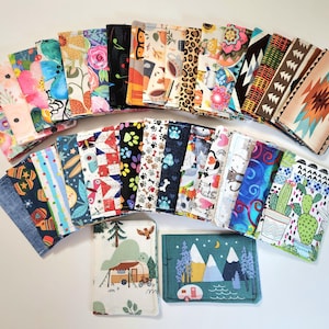 May include: A collection of rectangular fabric pouches featuring a wide variety of colorful patterns, including floral prints, animal motifs, geometric shapes, cactus designs, and outdoor scenes with campers and mountains, all arranged in a fan layout.