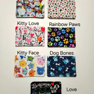 May include: Seven rectangular fabric card holders featuring various patterns: Happy Cats, Tiny Paws, Kitty Love, Rainbow Paws, Kitty Face, Dog Bones, and a black Love My Dog holder with the text Be the person your DOG thinks you are LOVE My.