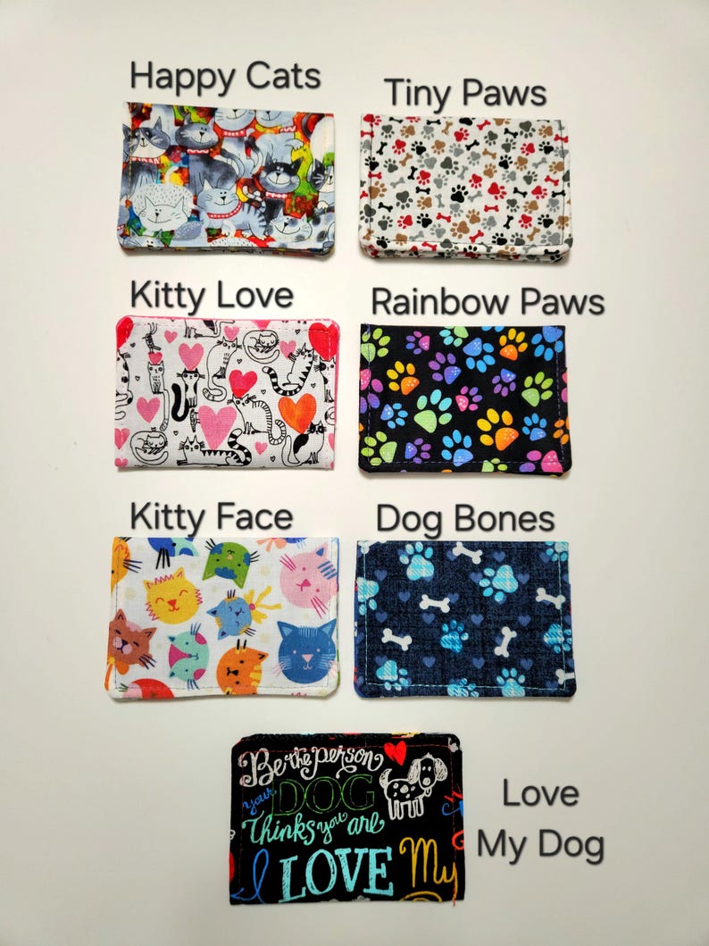 May include: Seven rectangular fabric card holders featuring various patterns: Happy Cats, Tiny Paws, Kitty Love, Rainbow Paws, Kitty Face, Dog Bones, and a black Love My Dog holder with the text Be the person your DOG thinks you are LOVE My.