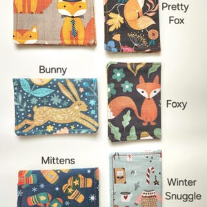 May include: Six rectangular fabric card holders featuring distinct patterns: Mr Fox with foxes in hats, Pretty Fox with a fox and flowers, Bunny with a rabbit, Foxy with a fox and leaves, Mittens with winter gloves, and Winter Snuggle with sweaters.