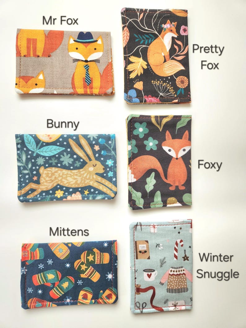 May include: Six rectangular fabric card holders featuring distinct patterns: Mr Fox with foxes in hats, Pretty Fox with a fox and flowers, Bunny with a rabbit, Foxy with a fox and leaves, Mittens with winter gloves, and Winter Snuggle with sweaters.