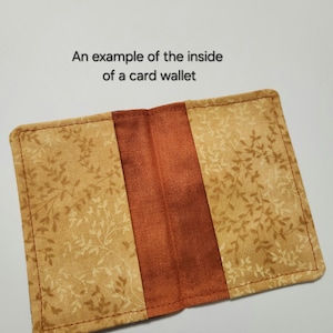 May include: A rectangular card wallet featuring a tan fabric with a brown leaf pattern on the outer panels and a solid rust-colored fabric in the center. The text "An example of the inside of a card wallet" is printed above the open wallet.