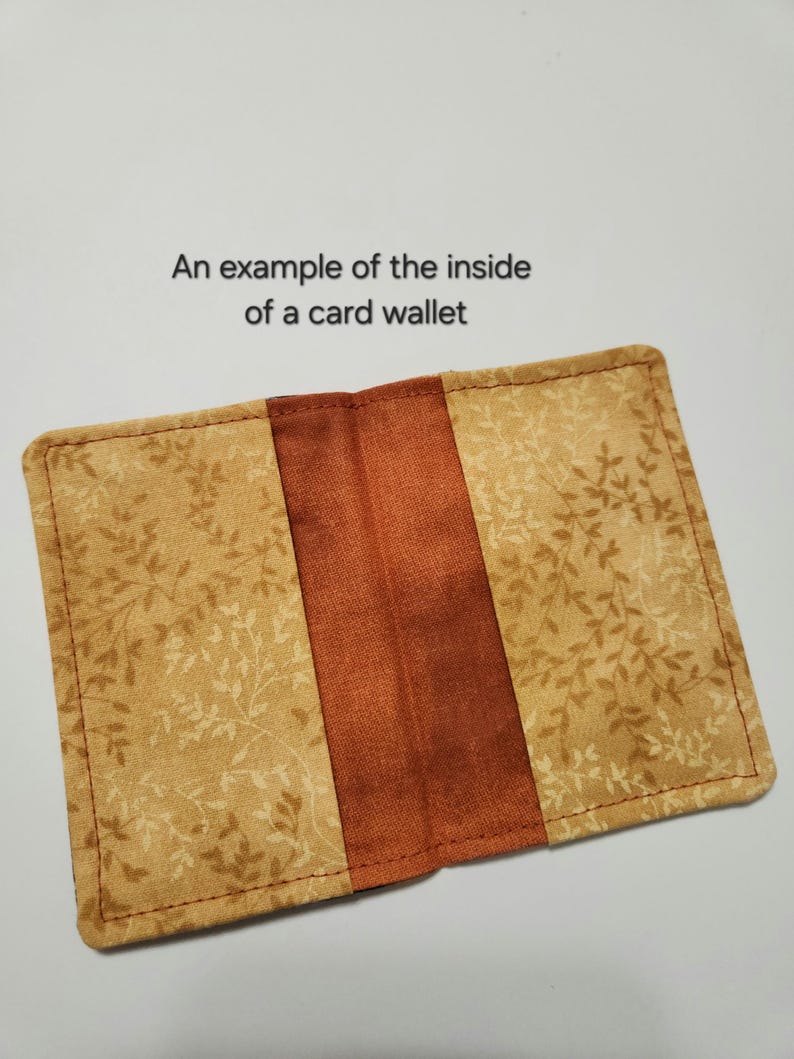 May include: A rectangular card wallet featuring a tan fabric with a brown leaf pattern on the outer panels and a solid rust-colored fabric in the center. The text "An example of the inside of a card wallet" is printed above the open wallet.