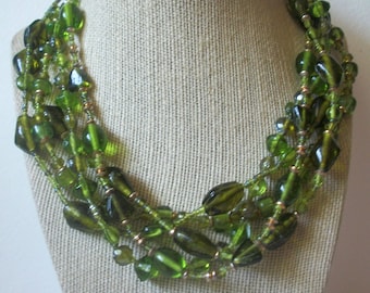 May include: A multi-strand necklace made of green glass beads of various shapes and sizes. The necklace is layered and features a mix of small and large beads.