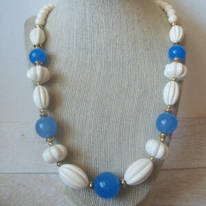 May include: A white and blue beaded necklace with gold accents. The necklace features alternating white oval beads with a textured surface and blue round beads.