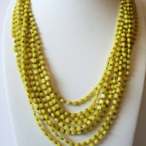 May include: A multi-strand necklace featuring several layers of small, round, bright yellow beads. The beads are strung on thin, metallic-colored wire, creating a cascading effect that hangs in concentric loops around the neck area.