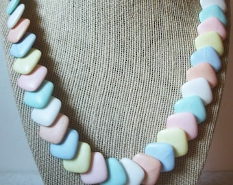 May include: A necklace featuring a series of smooth, square-shaped beads in a repeating pastel color palette of soft pink, pale blue, creamy yellow, and white. The beads are arranged in a single strand, creating a uniform and colorful pattern.
