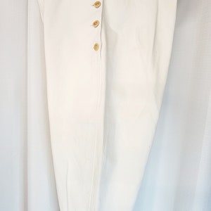 May include: White cotton pants with a button fly and a buckle strap at the bottom. The pants are hanging on a white hanger.